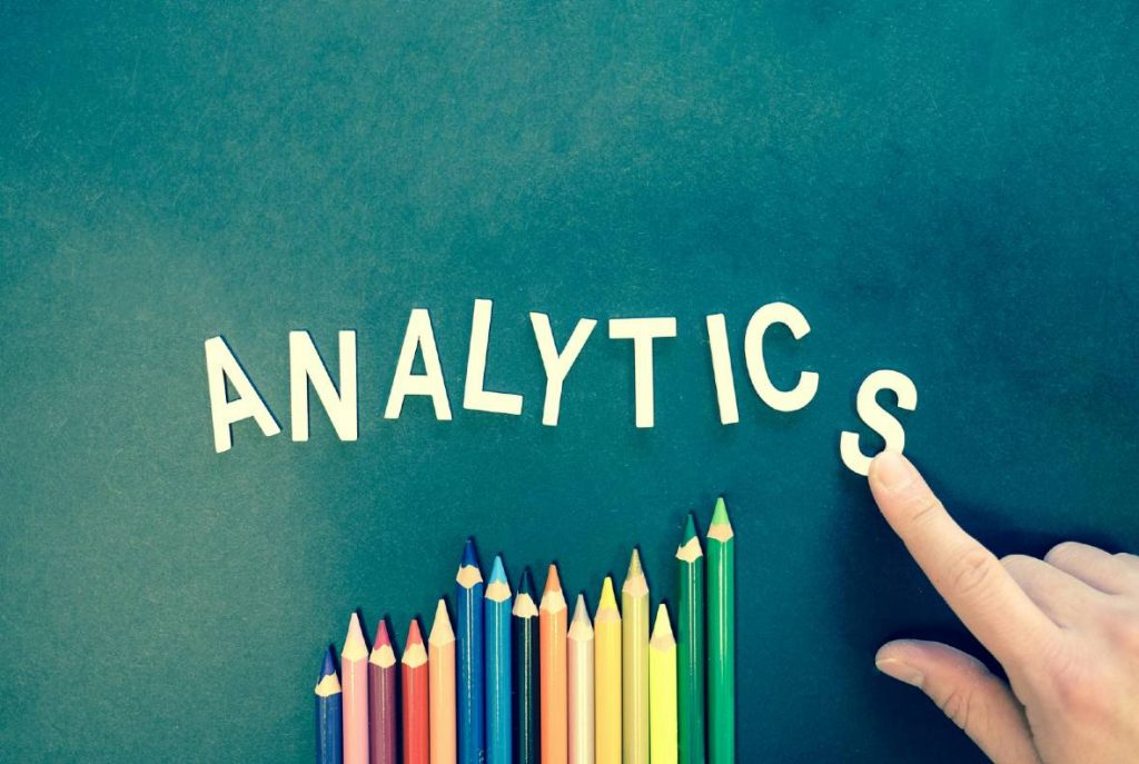 A finger writes the letters 'Analytics' on a black board. Marketing analytics and dashboard services for Charity Digital Marketing